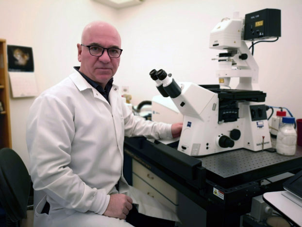 Prof. Alp Can in front of a ZEISS microscope.